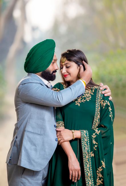 A man and woman sharing an intimate moment outdoors, with the man gently holding the woman's face and the woman smiling softly. The man is wearing a light grey suit and a vibrant green turban, while t